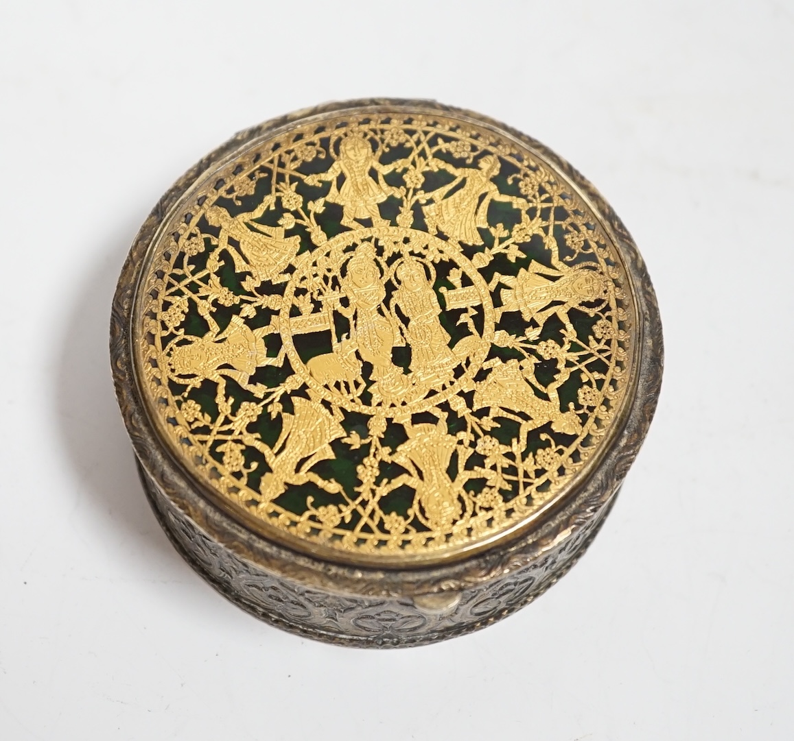 An Indian? embossed white metal circular box, with gilt and enamelled hinged cover decorated with Indian dancers, diameter 73mm.
